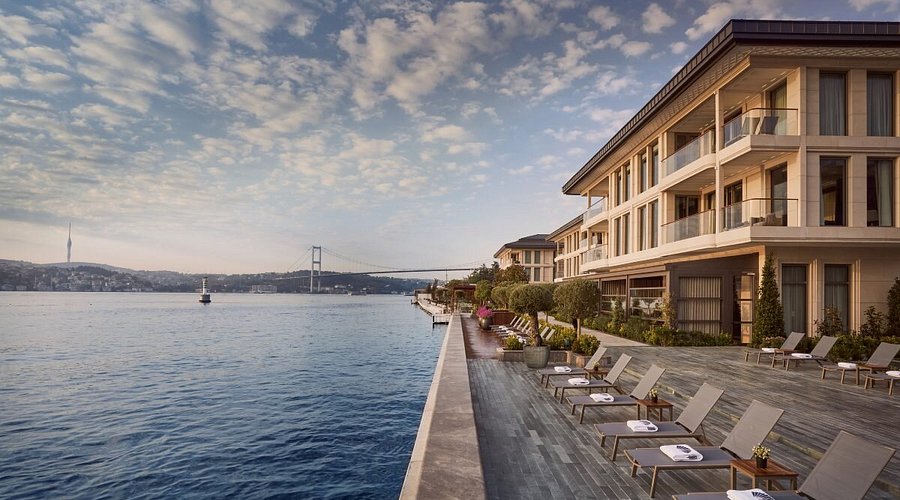 Aerial waterfront view of Mandarin Oriental Bosphorus Istanbul at sunset, showcasing the sprawling luxury resort architecture and private boat docks on the Bosphorus.