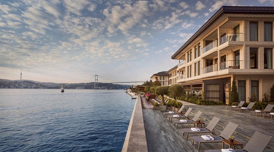 Aerial waterfront view of Mandarin Oriental Bosphorus Istanbul at sunset, showcasing the sprawling luxury resort architecture and private boat docks on the Bosphorus.